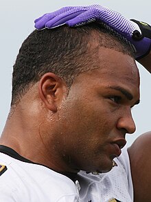 A gridiron football player places his hand on his head while sweat drips down his forehead and around his ear.