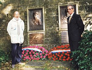 Zwei Männer in festlicher Kleidung stehen an einem Denkmal.