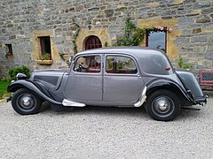 Une Citroën Traction 11 BL (Berline Légère) des années 1950, dans une belle et rutilante livrée grise métallisée avec les ailes noires.