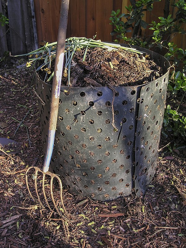 A pitchfork with five tines next to a compost bin. In this configuration, the pitchfork resembles a garden fork.
