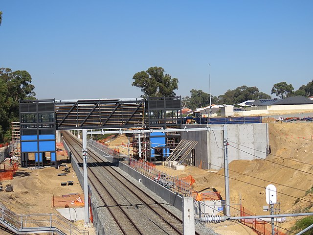 View from a bridge of a dual-tracked railway line with concrete retaining walls and a metal concourse under construction