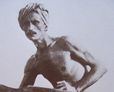 Photographie en noir et blanc d'un homme torse nu, coiffé d'un foulard.