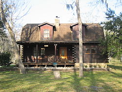 Front view of two-story log house in summer, with porch and dormer roof