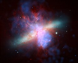 La nébuleuse Messier 82. Image composite en fausses couleurs, réalisée à partir de données de Chandra, Spitzer et du téléscope Hubble (HST). Le spectre colorimétrique a été compressé pour l’amener dans le domaine visible : la lumière infra-rouge enregistrée par Spitzer apparait en rouge, la lumière visible émise par l’hydrogène et enregistrée par Hubble apparait en orange, la lumière visible à courte longueur d’onde (couleur réelle bleu-violet) apparait en jaune-vert, les rayons X enregistrés par Chandra apparaissent en bleu. (définition réelle 4 299 × 3 490)