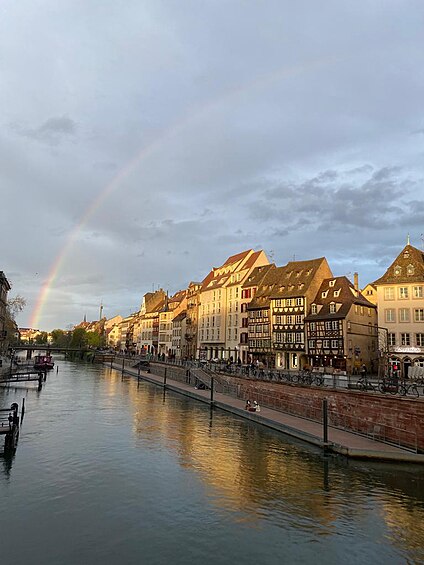 Picture of the beginning of a rainbow in Strasbourg taken from a bridge. The bridge is not visible, the river on which it has been built is however.