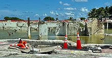 Des murs en béton dont il ne reste que la base et des armatures métalliques, dépassant d’une zone inondée.