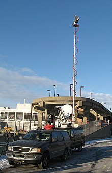 TV news production truck doing a remote broadcast at New York Passenger Ship Terminal. The tall telescoping antenna is pointed at a receiving antenna on the Empire State Building, allowing the truck to send video by microwave link to the production facility. TV remote pickup Pier 88 jeh.JPG