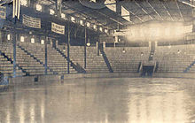 Black and white image of the arena's interior, including the ice, seating area, and windows letting in sunlight