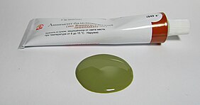 Sur un plan horizontal, un tube de pommade blanc et quelques millilitres de son contenu, de couleur vert argile.