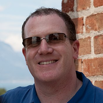 39 year-old man with sunglasses looking towards the camera.