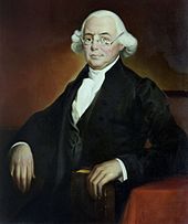 Ein sitzender sitzender James Wilson mittleren Alters in einem schwarzen Anzug, einem weißen Halstuch und einer weißen Perücke.