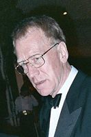 A long-faced man in a suit; he wears spectacles and his short-cropped hair is greying at the edges.