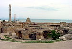 A picture of several deteriorating stone structures, with two thin cylindrical towers of varying heights standing to the left of the background.