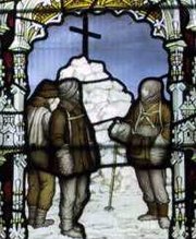 Three figures are depicted in coloured glass, standing by a cairn of snow topped by a large cross. The scene is framed by a decorative arch.