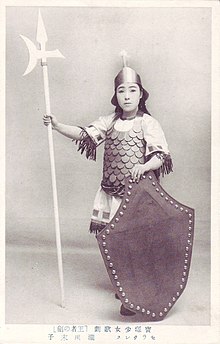 Carte postale en noir et blanc représentant une femme déguisée en soldat, armé d'une hallebarde.