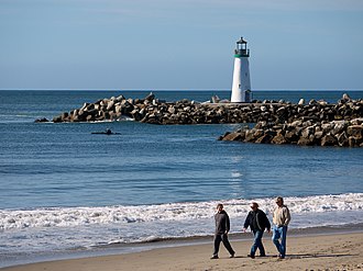 People walking on the beach, with Walton Lighthouse in the background Walking on the Beach (8508502117).jpg