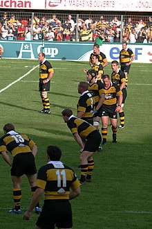 Alignement de dix joueurs en maillot rayé jaune et noir derrière un onzième joueur.