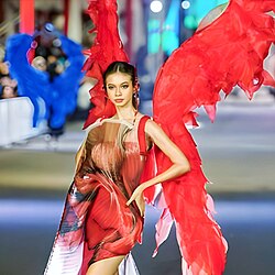 Yuki Kato wearing a fanciful dress on a fashion runway, left arm akimbo, looking slightly left of camera