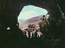 Photographie de l'entrée d'une grotte avec des visiteurs.