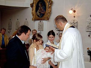 A Roman Catholic priest baptizes an infant as ...