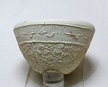 Photographie d'un bol à décor de pampres et de grenades avec inscription en arabe, céramique argileuse à décor moulé de Suse des VIIe – VIIIe siècles, musée du Louvre