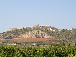 Photo shows a large hill topped with castle walls