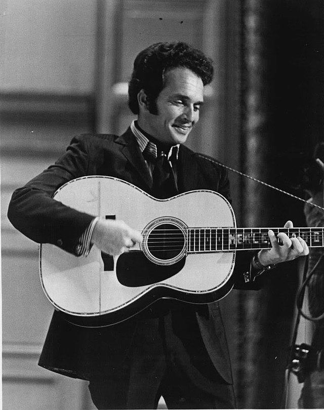 A dark-haired man wearing a dark jacket, playing a guitar