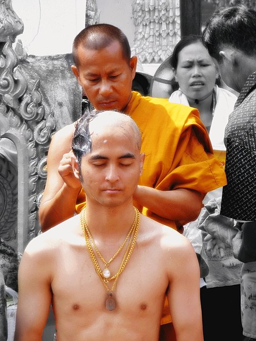 A Thai Buddhist monk shaving the head of a man preparing to also become a Buddhist monk; this is known as tonsure