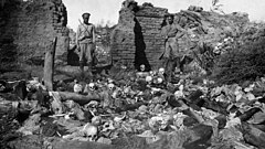Photograph of two Russian soldiers in a ruined village looking at skeletal remains