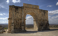 Вид триумфальной арки с двумя вставными колоннами с каждой стороны, между которыми находятся ниши, и с длинной табличкой сверху, на которой написана надпись