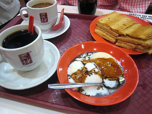 Kopi (pictured in the background, or Kopi O (pictured in the foreground), paired with kaya toast is a popular breakfast option in Singapore.