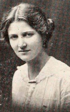 A young white woman with light hair parted center and dressed back to the nape; she is wearing a white blouse or dress with a frill-trimmed collar and placket
