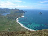 Foto eines Strandabschnittes von einem Berg aus fotografiert, im Vordergrund ein Dorf, im Hintergrund Berge, rechts im Bild das Meer und eine Insel