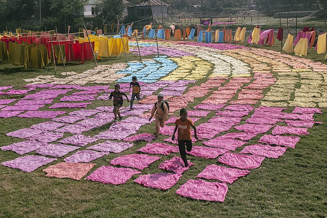 图为在正在晒干中的各色布料中玩耍的孩子。
