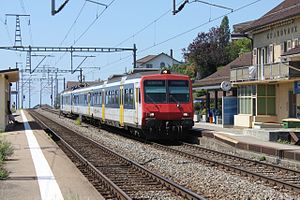 Biru dan putih dengan kereta merah depan pada double-track jalur kereta api yang dikelilingi oleh platform