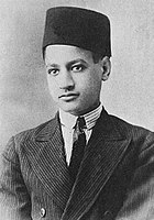 A boy wearing a jacket, a white shirt with a black tie and a fez on his head