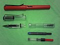 Lamy Safari (top) in red and Vista (bottom) fountain pens. Under the Lamy Vista transparent demonstrator pen a Lamy T10 ink cartridge and a Lamy Z 24 piston operated converter for using bottled fountain pen ink.