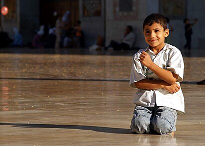 A boy kneeling in the courtyard of the Great Umayyed Mosque in Syria Playful boy in the expansive courtyard of the Great Umayyed Mosque of Damascus, Syria.jpg