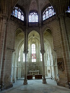 Chapelle contenant du mobilier en bois et un groupe sculpté accroché au mur de droite, surmontée de trois vitraux décoratifs.