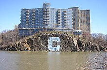 Blick über den Spuyten Duyvil Creek. Auf der anderen Seite befindet sich der Stadtbezirk Bronx mit dem Stadtteil Riverdale. Auf der Wand befindet sich seit etwa 50 Jahren das Logo der Columbia University.