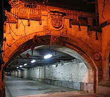 Südeingang der Nebenunterführung. Am Bahnsteig steht ein Zug, auf dem Schlussstein ist das Breslauer Wappen sichtbar, daneben Spuren des nach dem Krieg entfernten Schriftzugs „DURCHGANG ZUR FLURSTRAßE“ (2005)