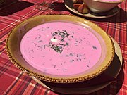 A bowl of bright pink soup sitting on a plaid tablecloth.