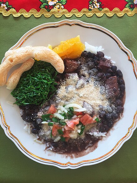 A plate of feijoada in Minas Gerais with traditional accompaniments: rice, fried collard greens (couve), cassava flour crisps (biscoito de polvilho), orange slices, vinagrete (a mix of olive oil, alcohol vinegar, tomatoes, onions and sometimes bell peppers), and cassava flour (farinha).