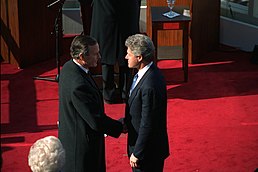 Fotografie George Bushe a Billa Clintona, kteří si podávají ruce těsně po zahajovacích ceremoniích v americkém Kapitolu.