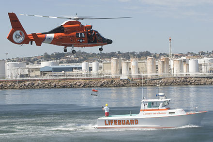 A United States Coast Guard (military) HH-65 Dolphin Helicopter demonstrates interagency Military-Civilian operations with a Los Angeles County Fire Department (civilian) Motor life boat