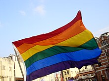 Colour photograph of a flag with six horizontal, coloured stripes of equal width: red, orange, yellow, green, blue & purple.