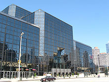 Un edificio de cristal tintado oscuro se alza sobre una calle de la ciudad.  Las esquinas del edificio se suavizan en ángulos de 45 grados.