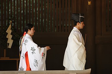 A kannushi wearing a jōe being accompanied by two miko