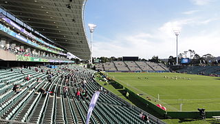 vue d'un stade depuis une tribune avec au centre de l'image la pelouse et au fond une autre tribune non couverte