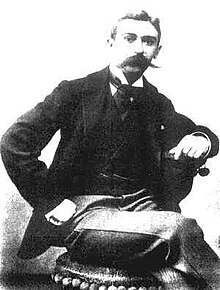 photographie en noir et blanc d'un homme moustachu, assis